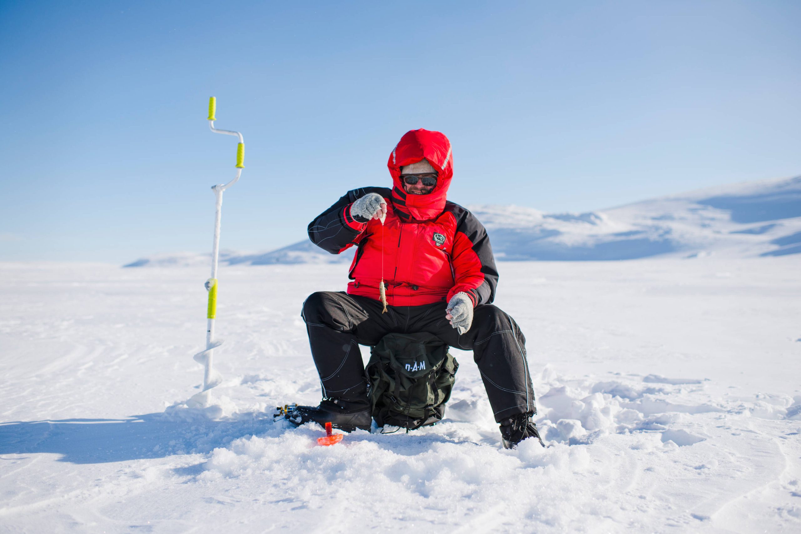 Man fishing in snowy environment, on top of the ice